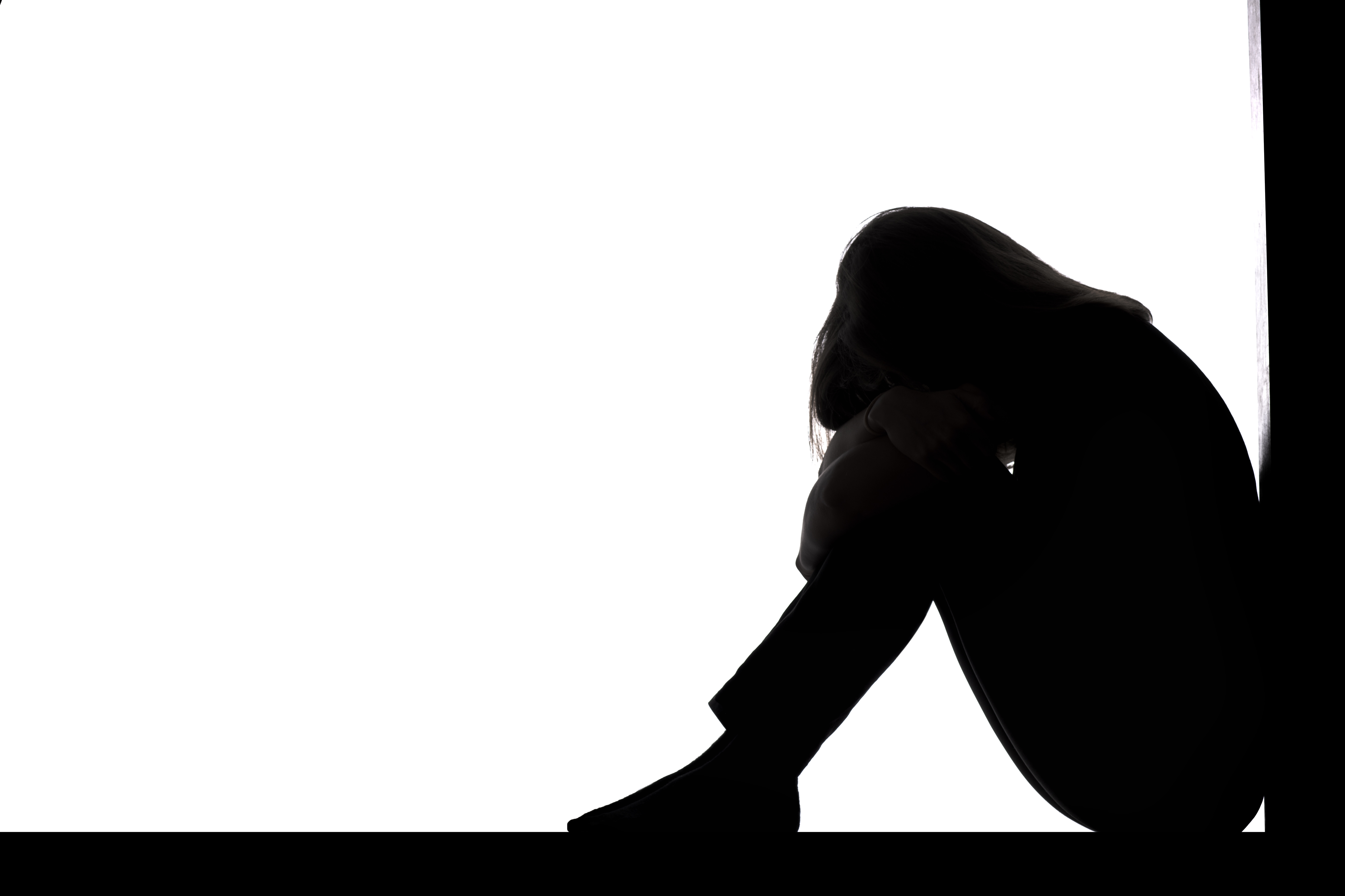 silhouette of a woman sitting on the floor in a corner on a white