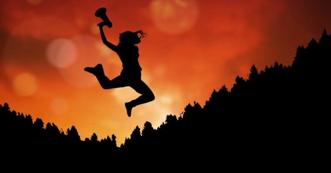 Businesswoman holding megaphone while jumping on mountain during sunset
