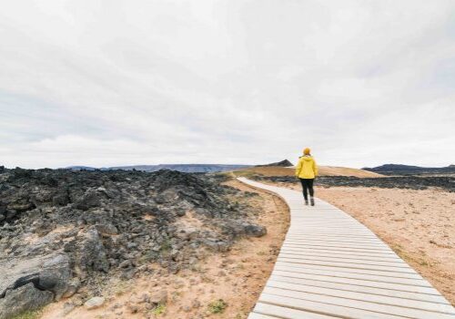 Woman in yellow raincoat walking in Krafla volcano lava field around Leirhnjukur mountain peak, Iceland.