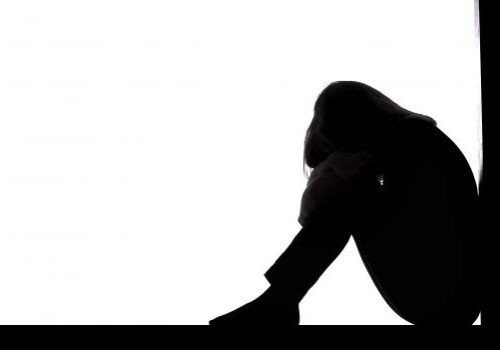 silhouette of a young woman sitting on the floor in a corner on a white isolated background, a sad girl crying putting head on knees,concept depression